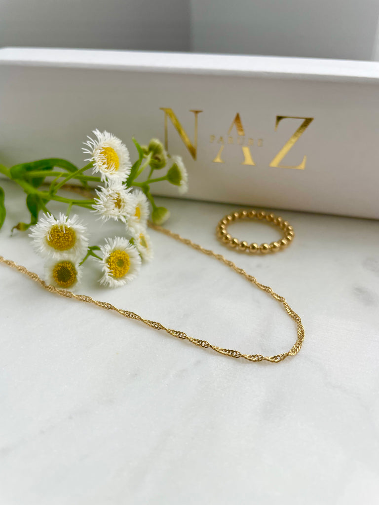 Gold filled Fine rope chain laying flat with beads of gold ring on marble with flowers and NAZ Parure Box in background