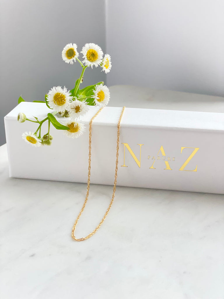 Gold filled Fine rope chain on marble with flowers laying against a NAZ Parure Box.