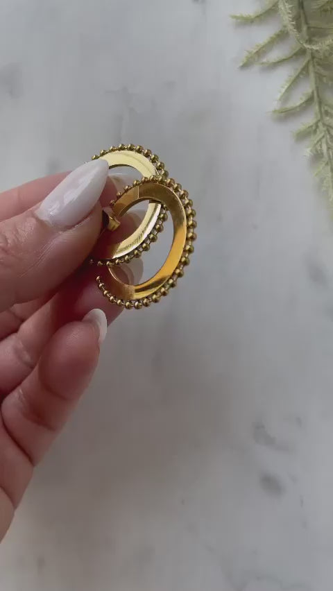 Woman with white manicure holding Beaded & Solid Hoop Earrings against a marble background.