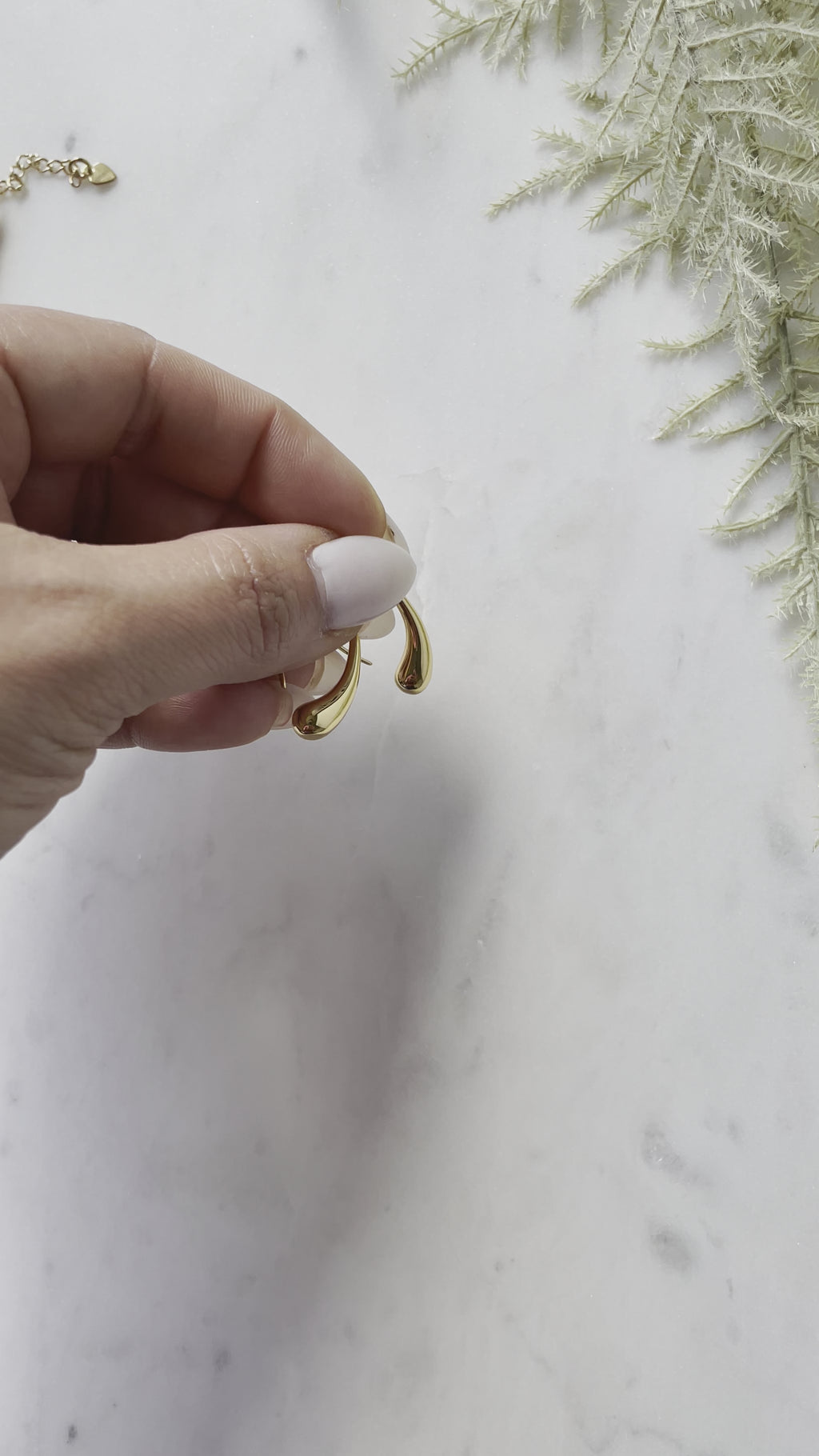 Woman with white manicure holding sterling silver waterdrop earrings against a marble background.