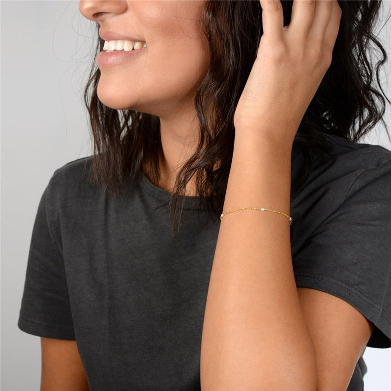 woman with gray t-shirt playing with hair to show gold filled pearls and chain bracelet on wrist.