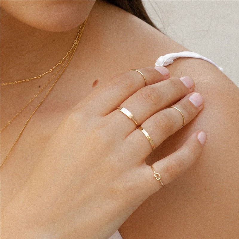 Woman with white tank top wearing multiple gold filled items including gold filled infinity band and gold filled knot ring from NAZ Parure.