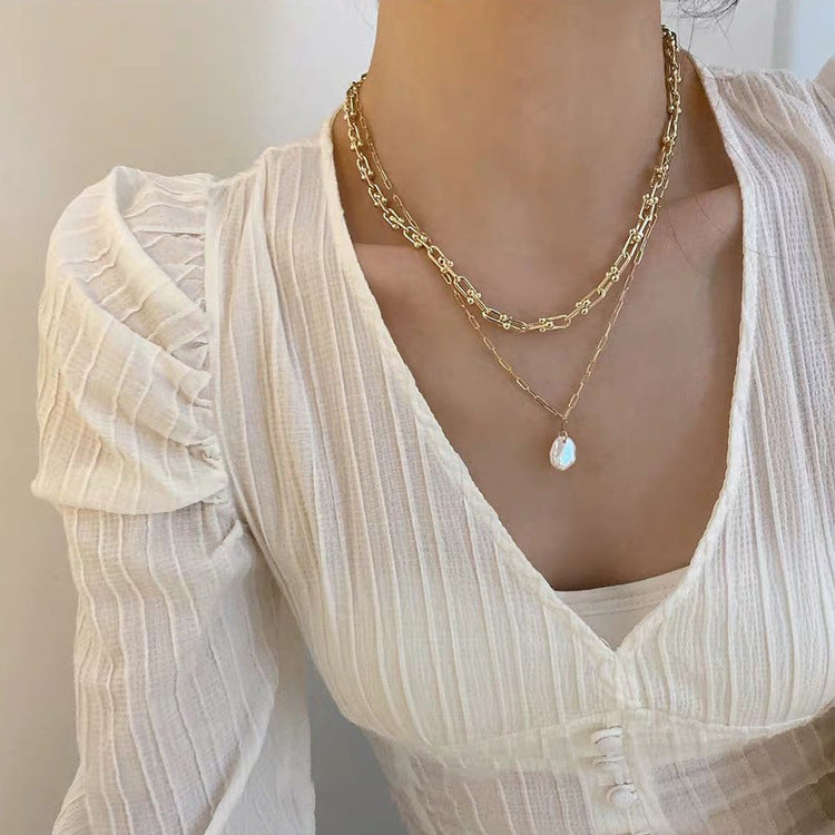 Woman in cream blouse wearing Shell Drop Paperclip Chain & Bold Gold Chain from NAZ Parure Jewelry. 