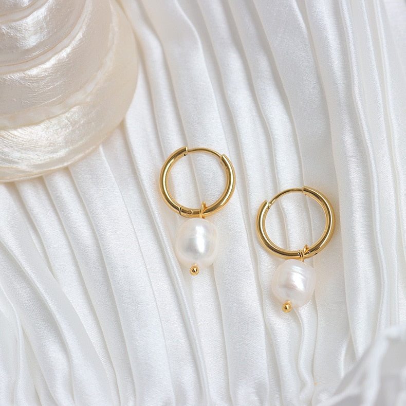 Elegant Pearl Drop Gold Hoops against a white satin fabric.