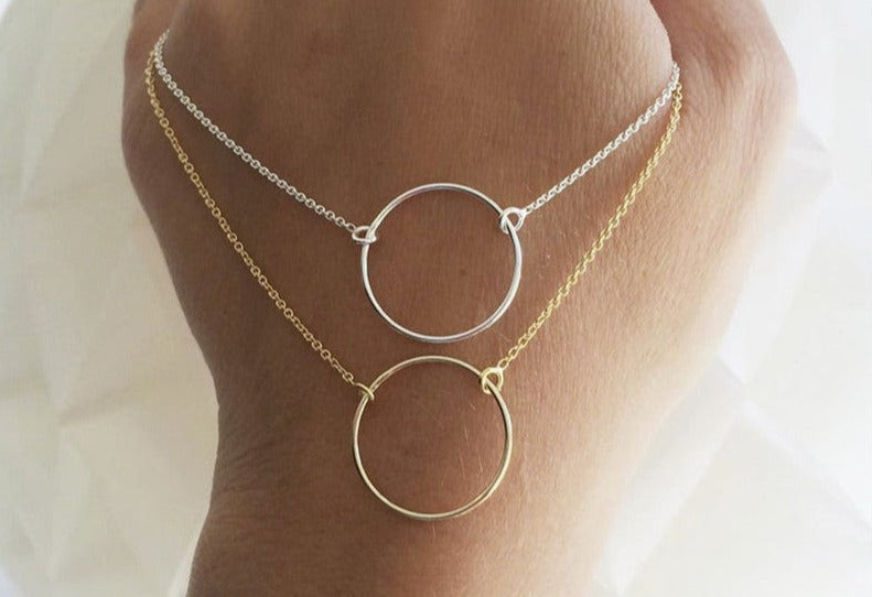 Hand holding both 14K gold plated & sterling silver Karma Necklaces from NAZ Parure Jewelry