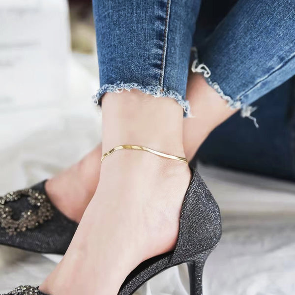 Woman with trendy jeans and black stilettoes wearing 18K gold vacuum plated Herringbone Anklet on stainless steel from NAZ Parure Jewelry.