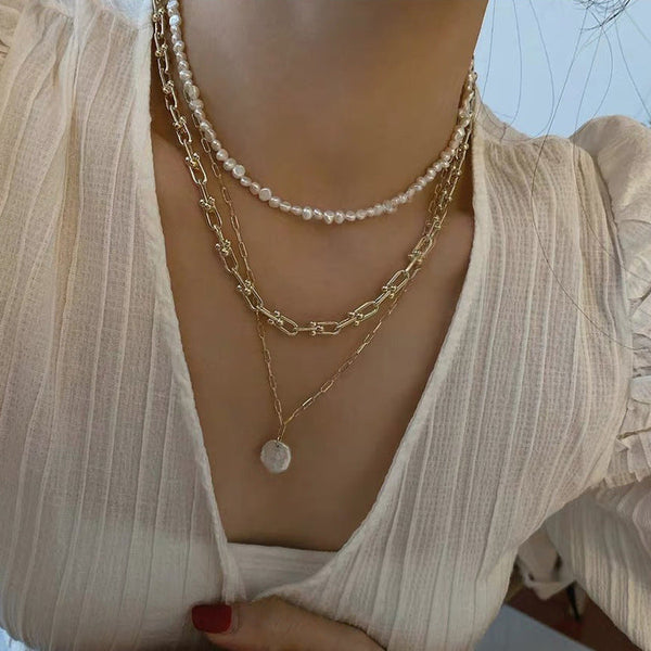 Woman in cream blouse wearing Shell Drop Paperclip Chain, Parure of Pearls choker & Bold Gold Chain from NAZ Parure Jewelry. 