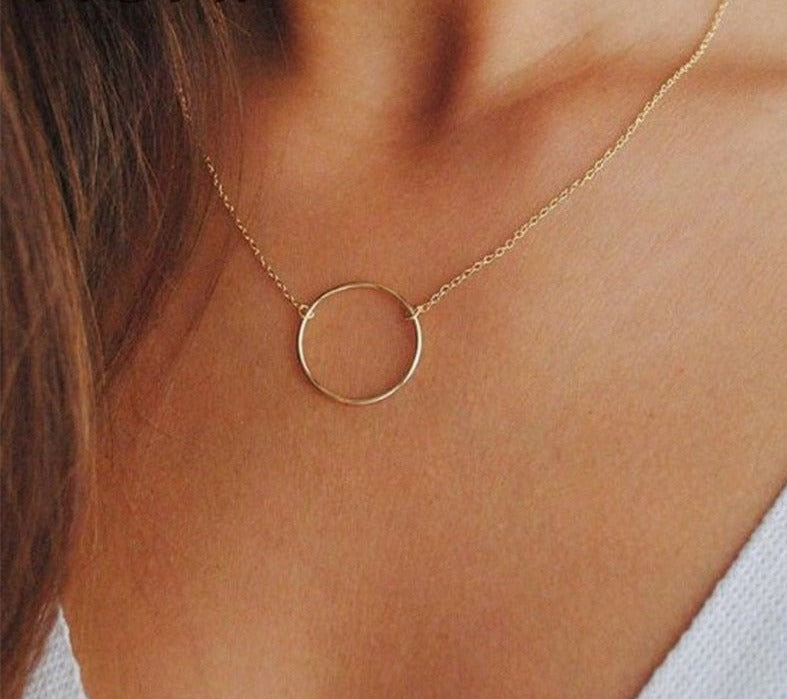 Woman wearing 14K gold plated Karma Necklace on a low cut white shirt. 