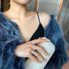 Woman in fancy blue fur coat wearing our White Opal Leaf Ring while holding a white clutch.
