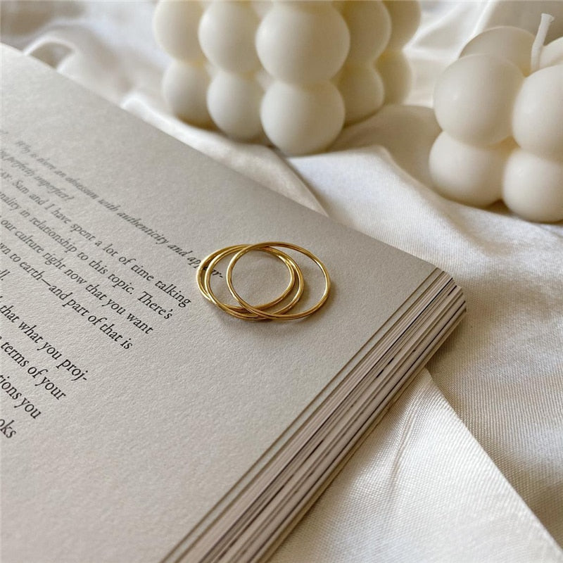Three 14K Gold-filled Simply Thin rings resting on book pages with white candles in background.