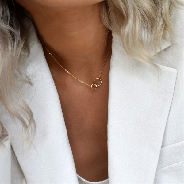 woman with low cut blouse and white blazer wearing 14K gold filled infinity necklace.