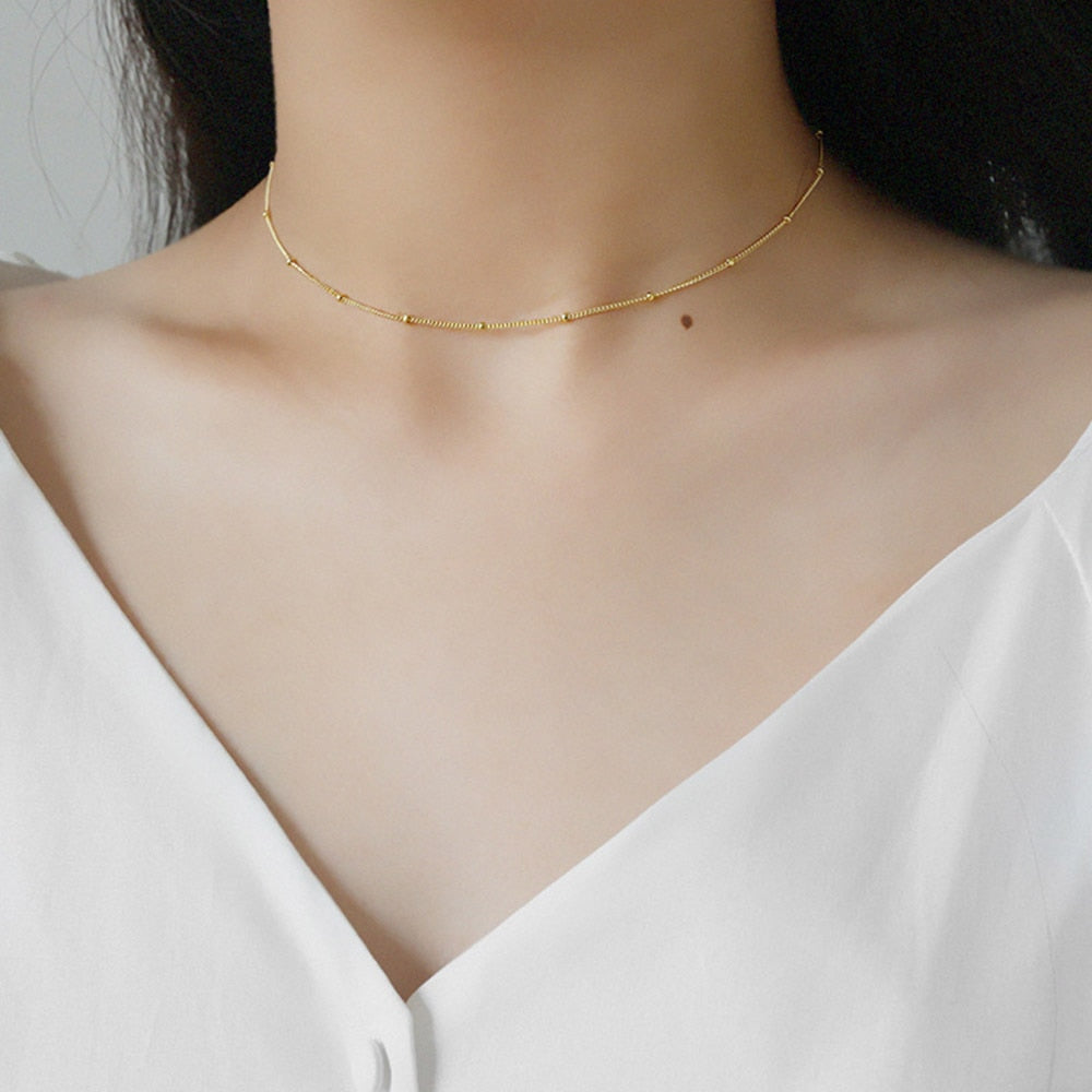 Woman with low cut white linen shirt wearing 18K gold plated Thin Beaded Choker from NAZ Parure Jewelry.