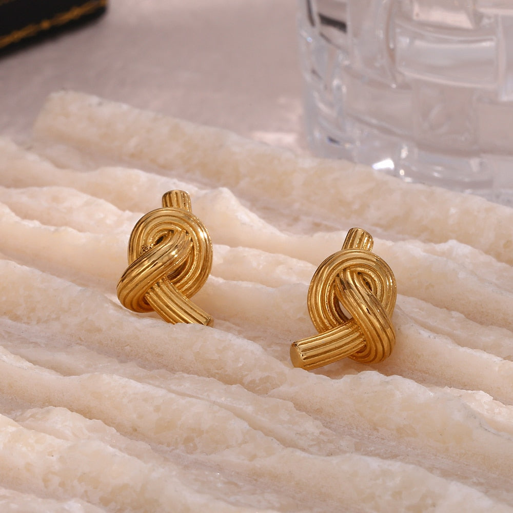 Timeless Knot Gold Studs resting on velvet fabric. 