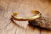 gold plated Wheat Cuff Bangle against rock and wood background.