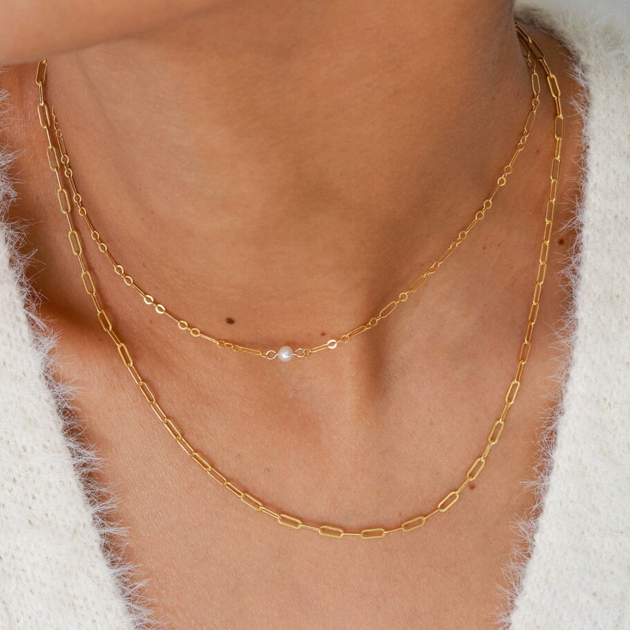 Woman in cashmere sweater wearing one gold filled Thin Figaro Single Pearl Necklace and one gold filled oval link chain from NAZ Parure.