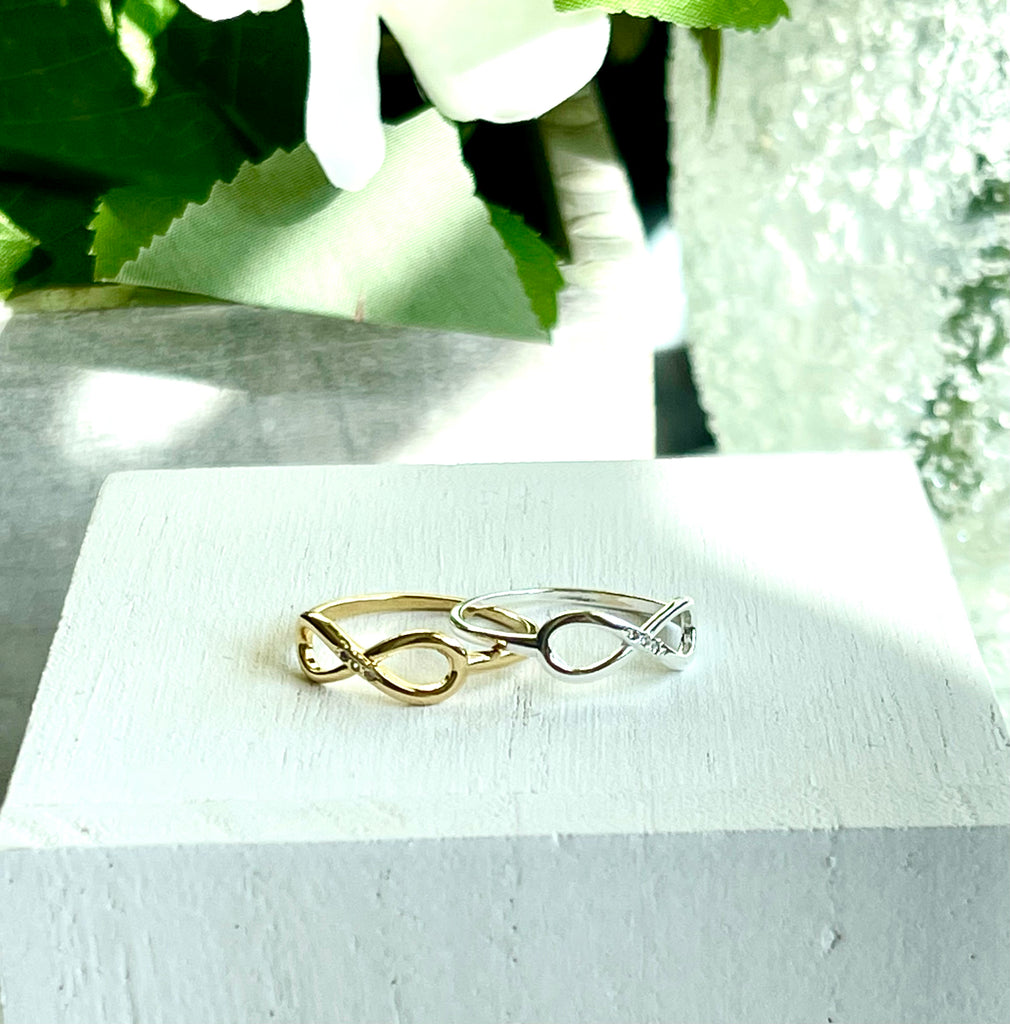 18K Gold FIlled and 925 Sterling Silver Infinity ring on white wooden block with greenery in background.