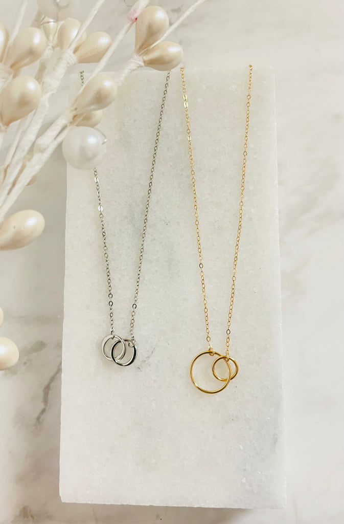 Interlock necklace and Infinity Necklace laying on marble stone.