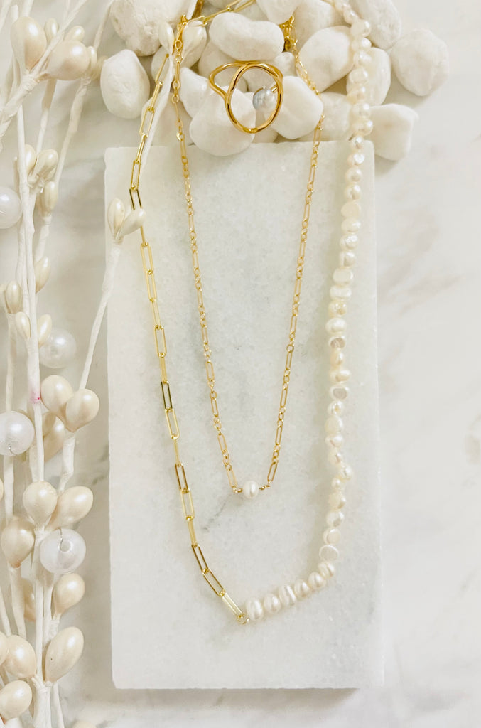 Gold Filled Figaro single pearl necklace resting on a white background with stones and flowers.