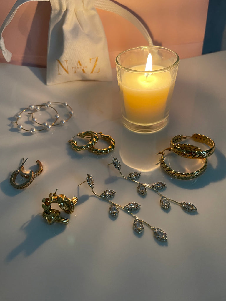 Gold wheat hoops and mulitple other earrings offered by NAZ Parure Jewelry with candle in background.