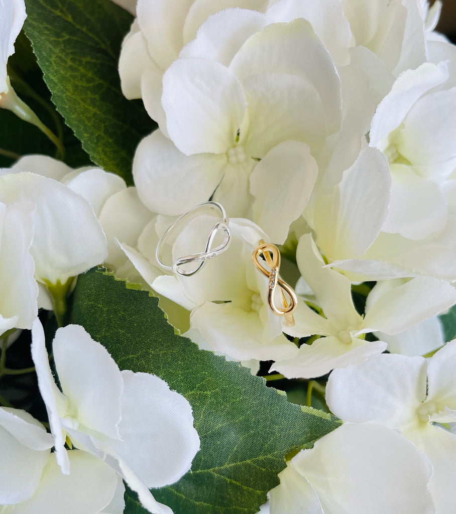 18K Gold Filled and 925 Sterling Silver Simply Infinity Ring resting on white flowers.